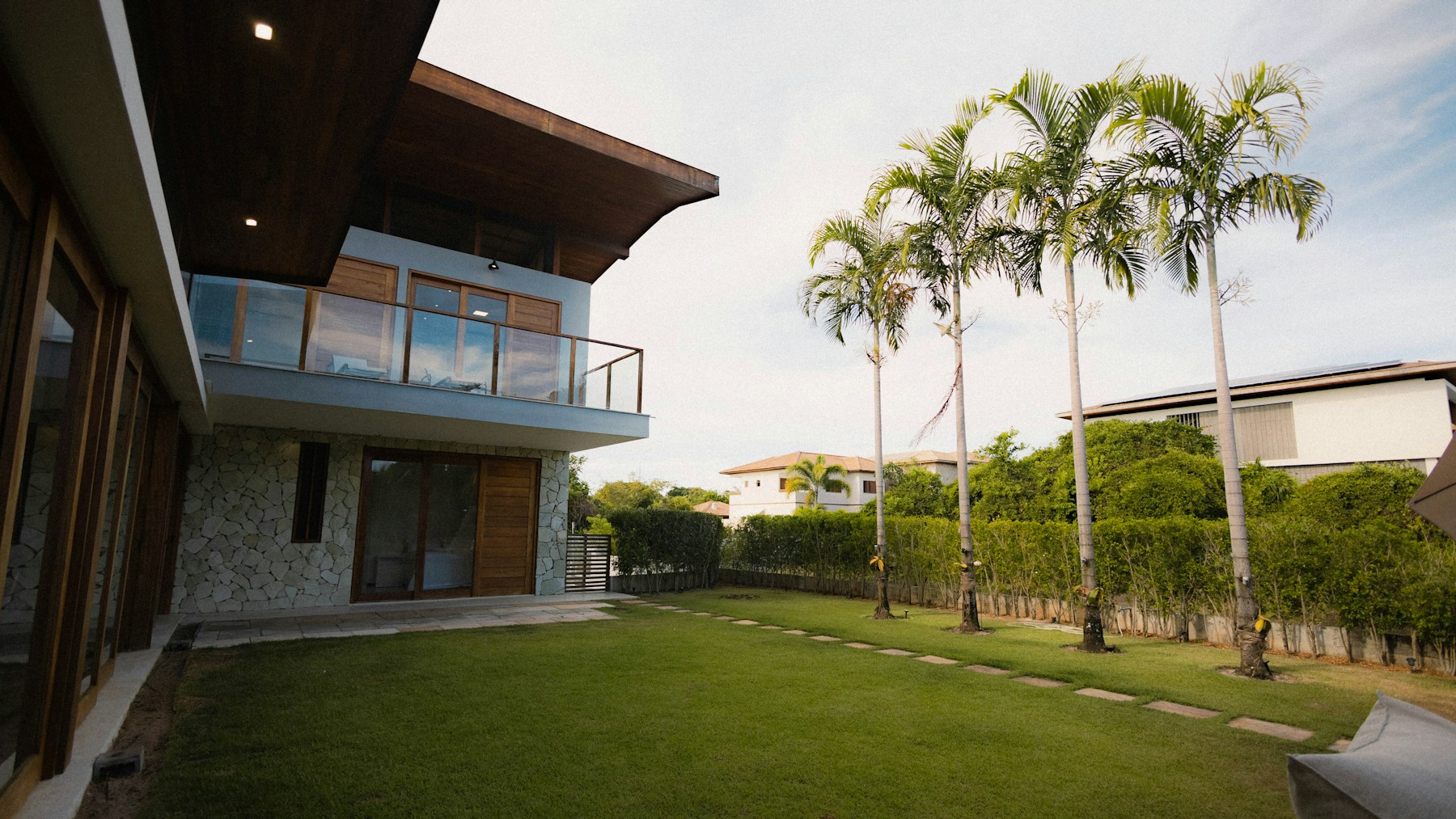 A sunlit home with a green lawn and palm trees
